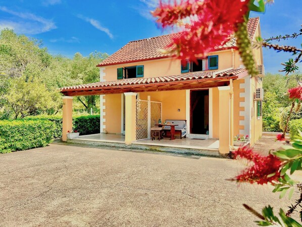 A two-story house with a tiled roof, a covered porch, and a garden.