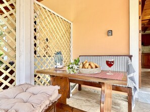 Uma mesa de madeira com uma cesta de pão trançada e um copo de vinho tinto, diante de uma parede cor de pêssego com padrão de treliça.