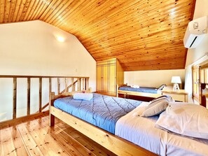 Quarto com teto de madeira, uma cama beliche, uma escrivaninha com abajur e um guarda-roupa.