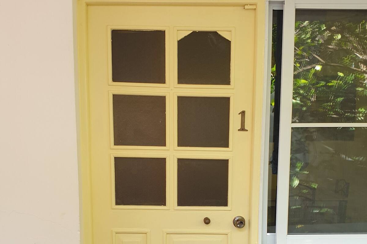 Una puerta amarilla con seis paneles de vidrio y el número '1', junto a una ventana con vistas a zonas verdes.