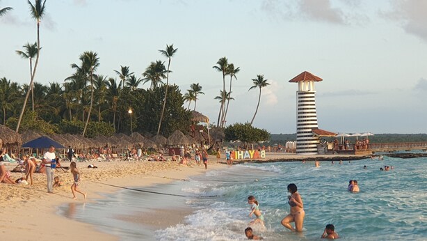 A beach with palm trees, a lifeguard tower, and people swimming. - PLAYA BLANCA BED & BREAKFAST (San Rafael del Yuma)