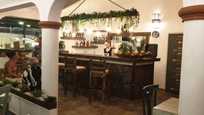 A bar area with wooden chairs, a bar counter with a fruit display, and shelves with bottles. - PLAYA BLANCA BED & BREAKFAST (San Rafael del Yuma)
