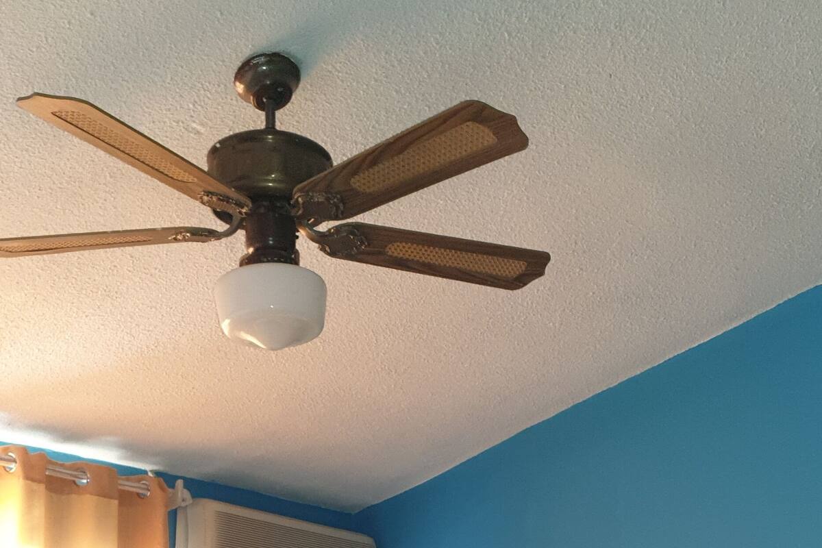 Un dormitorio con cama, ventilador de techo, equipo de aire acondicionado, espejo circular y cabecera con ventilador.