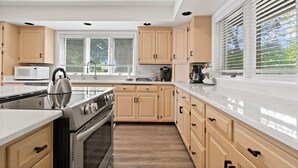 A modern kitchen with light wood cabinets, stainless steel appliances, and a large window with blinds. - Blue Water Beach House! Amazing Beach, sleeps 20! (Sanilac Township)