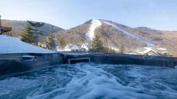 A hot tub with a mountain view, surrounded by buildings and trees.