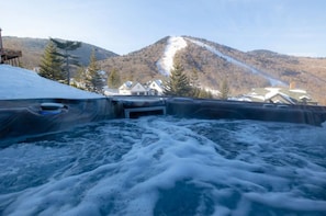 A hot tub with a mountain view, surrounded by buildings and trees.