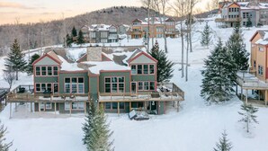 A multi-story building with a balcony and a covered area, surrounded by snow and trees.