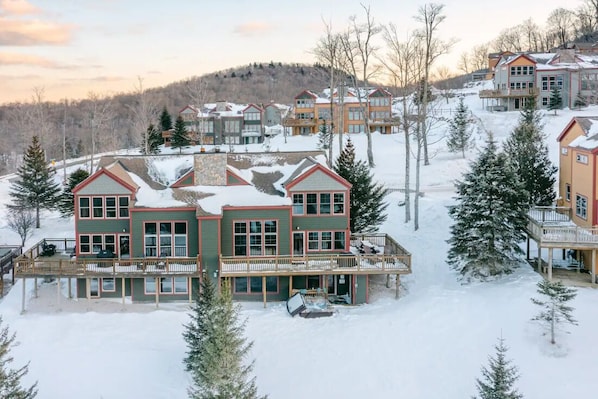 A multi-story building with a balcony and a covered area, surrounded by snow and trees.