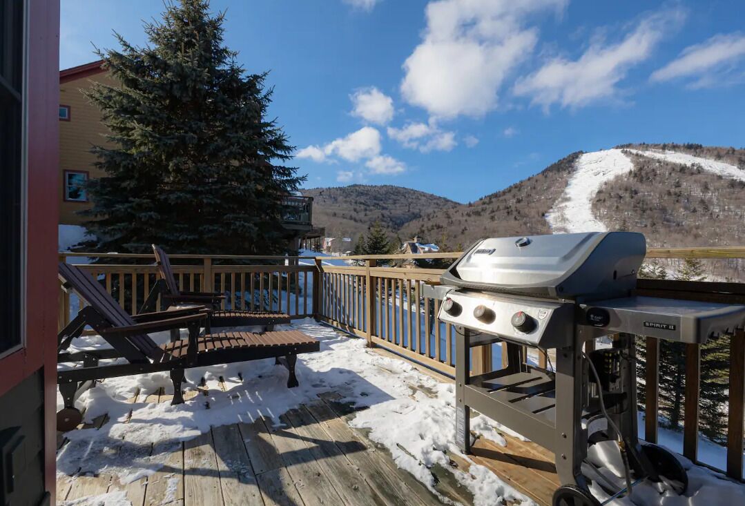 A deck with a grill, a wooden bench, and a view of a snowy mountain.