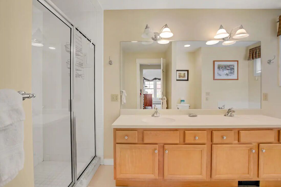 A bathroom with a glass shower enclosure, a large mirror, and wooden cabinets.