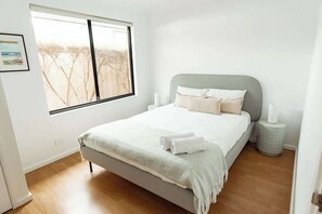 Ein Schlafzimmer mit Bett, Fenster, Nachttisch und einem Wandbild.