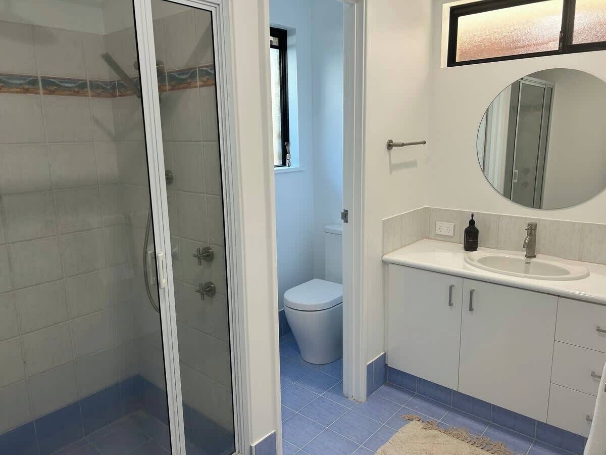 Baño con cabina de ducha de vidrio, inodoro, lavamanos con espejo y un ventanal pequeño.