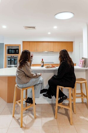 Two people seated at a kitchen island with a microwave, oven, and wine bottle visible.