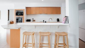 Una cocina moderna con armarios de madera, encimera blanca y tres taburetes de madera.