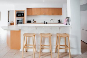 A modern kitchen with wooden cabinets, a white countertop, and three wooden stools.