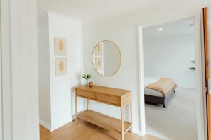 Una stanza con un tavolino da toilette in legno, uno specchio rotondo e un letto con coperta color beige.