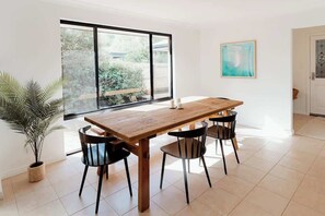A dining area with a wooden table and black chairs, a potted plant, and a large window with a view of greenery.