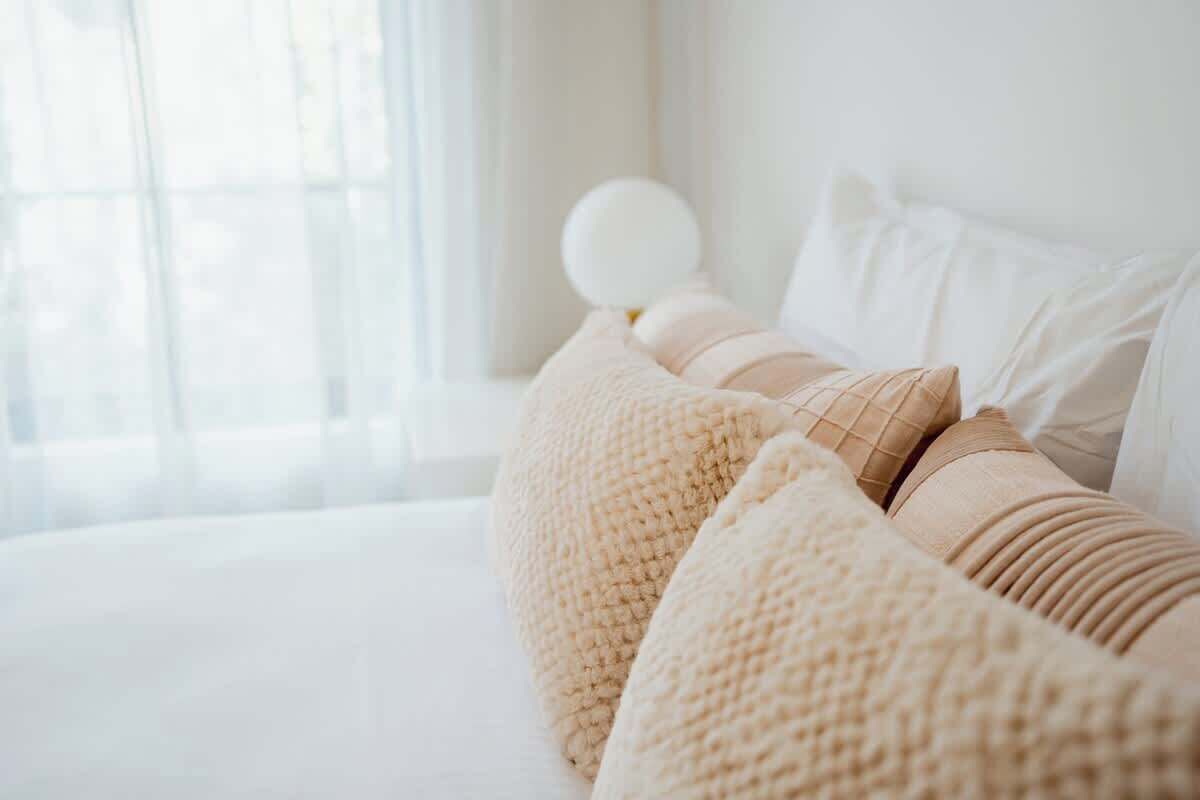 A neatly made bed with a white comforter and beige pillows.
