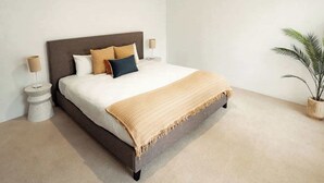 Un dormitorio con cama, lámparas de noche, mesita de noche y una planta en maceta.