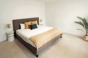A bedroom with a bed, bedside lamps, a bedside table, and a potted plant.