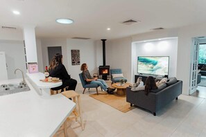 A modern living room with a fireplace, a television, and a kitchen area.