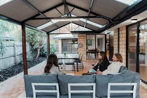 Un patio esterno con zona salotto coperta, tavolo da pranzo e vista sul giardino.