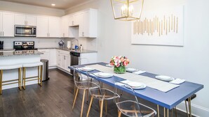 Una cocina moderna con armarios blancos, electrodomésticos de acero inoxidable y una mesa de comedor azul con sillas transparentes.