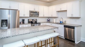 Una cocina moderna con armarios blancos, electrodomésticos de acero inoxidable, encimera de granito y una zona con taburetes de bar.