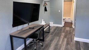 A modern room with a flat-screen TV mounted on the wall, a wooden desk with a chair, and a hallway leading to a bathroom. - 2 Room Suite - Indoor Pool and Spa - Walk to the Boardwalk - No Cleaning Fee! (Santa Cruz)