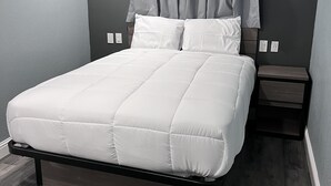 A modern bedroom with a bed, grey walls, and a wooden floor. - 2 Room Suite - Indoor Pool and Spa - Walk to the Boardwalk - No Cleaning Fee! (Santa Cruz)