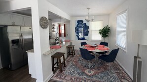 A modern kitchen with a stainless steel refrigerator, a dining area with a round table and blue chairs, and a patterned rug.