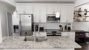 A modern kitchen with white cabinets, stainless steel appliances, granite countertops, and pendant lighting.