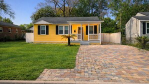 A yellow single-story house with a front porch, a brick driveway, and a small lawn.