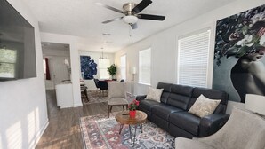 A modern living room with a dark sofa, a patterned rug, and a ceiling fan.