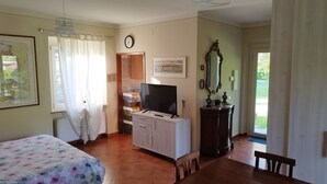 A hotel room with a bed, a TV on a wooden cabinet, a clock on the wall, and a view of the outside. - La Casina (Barga)