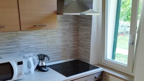 A compact kitchen with a microwave, coffee maker, and stove. It features wooden cabinets, a tiled backsplash, and a window with a view of greenery. - La Casina (Barga)