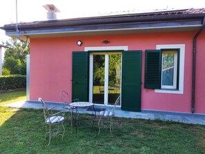 A pink house with green shutters, a door, and a small patio with two chairs and a table. - La Casina (Barga)