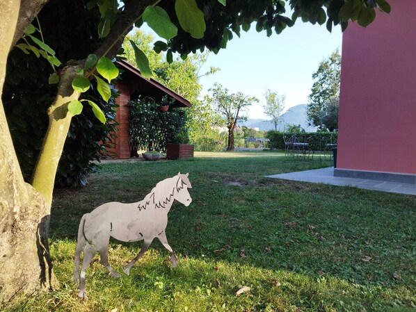 A white horse sculpture in a grassy area with a brick building and a pink wall in the background.