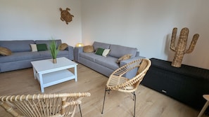 Una sala de estar con un sofá gris, una mesa de centro blanca, una silla de mimbre y una decoración de cactus.