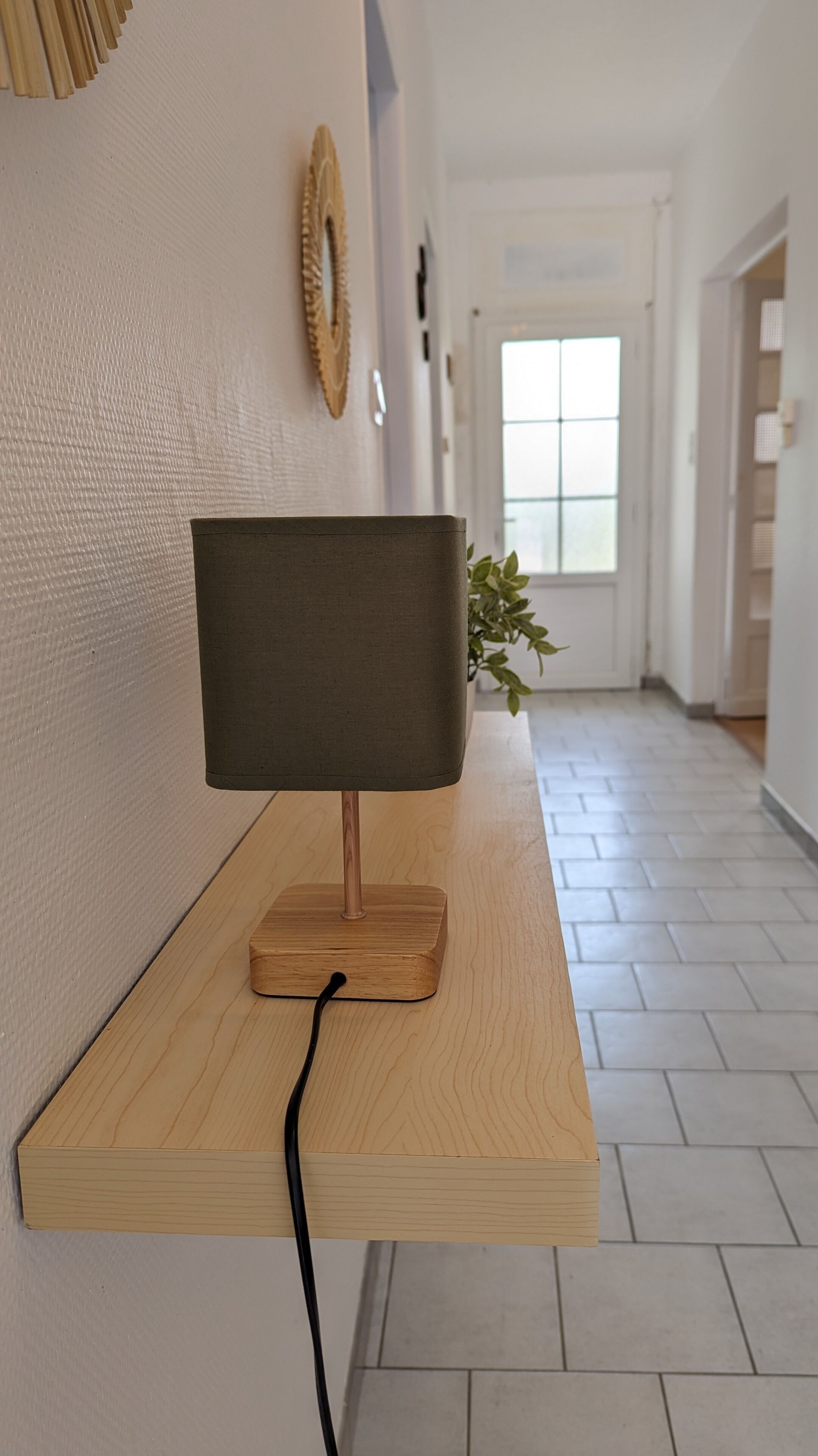 Una habitación moderna con un escritorio de madera, una lámpara de pared y una planta en maceta.