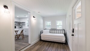 Quarto com cama, mesa de jantar com cadeiras e cozinha ao fundo.