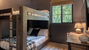 Ein Schlafraum mit Etagenbett, Fenster, Lampe und kleinem Tisch.