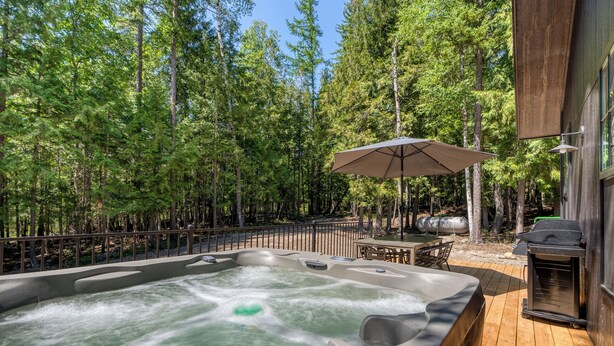 Ein Whirlpool, umgeben von einer Holzterrasse, mit Tisch und Stühlen, und einem Grill im Hintergrund.