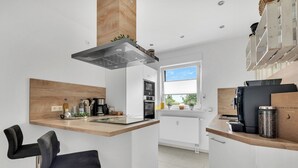 A modern kitchen with a central island, bar stools, a built-in oven, and a coffee machine. - 1 Bedroom Condo in Goslar (Goslar)