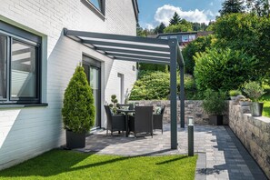 Un patio con una pérgola, una mesa de comedor con sillas y plantas en macetas.