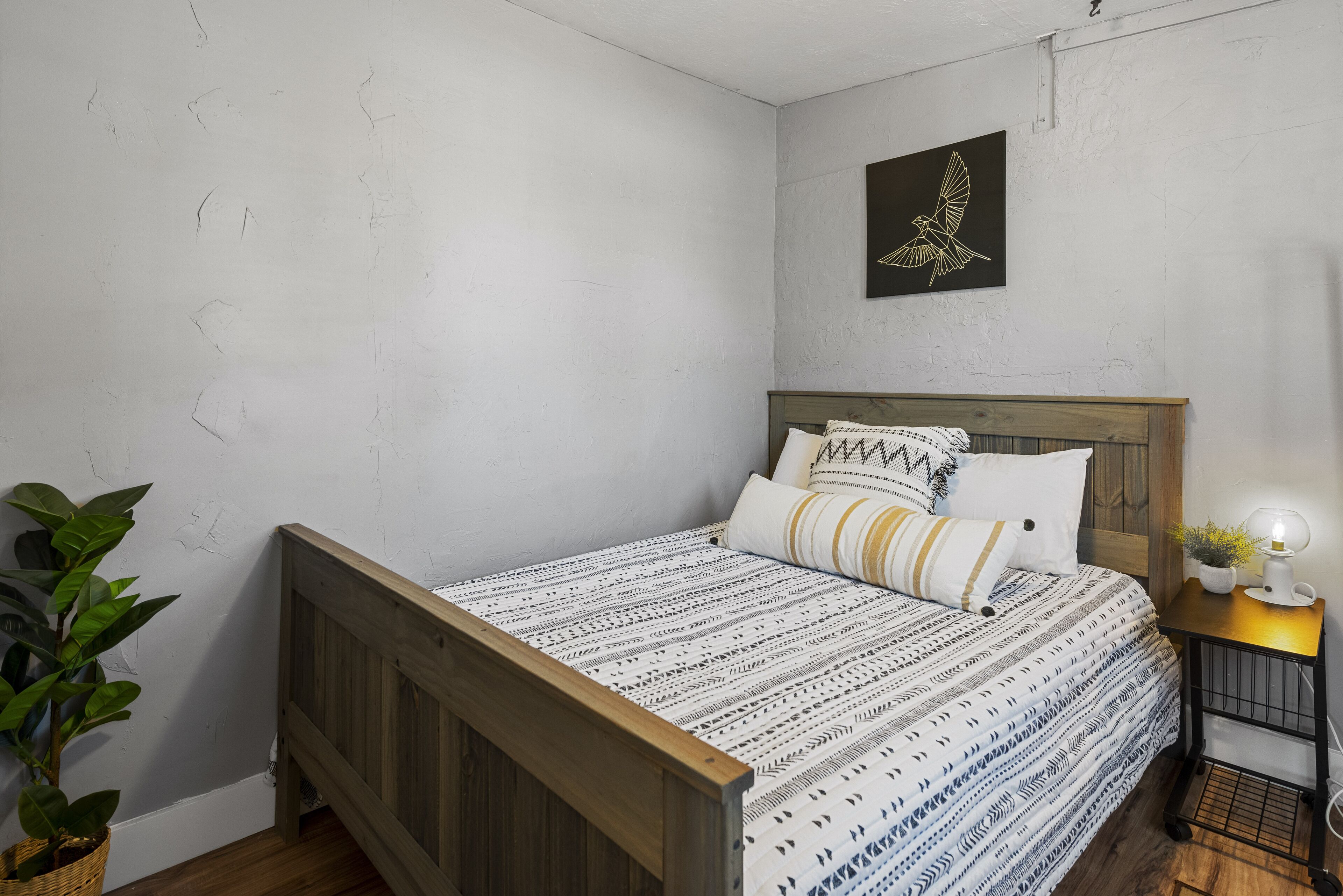 Un dormitorio con cama de madera, ropa de cama estampada, una lámpara de pared y una planta en maceta.