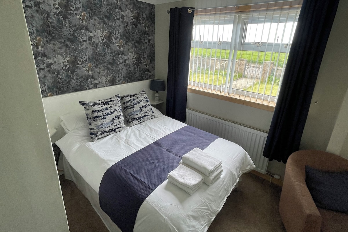 A bedroom with a bed, a window with curtains, a radiator, and a view of the outside.