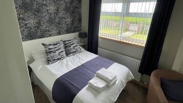 Ein Schlafzimmer mit Bett, einem Fenster mit Vorhängen, einer Heizung und Blick ins Freie.