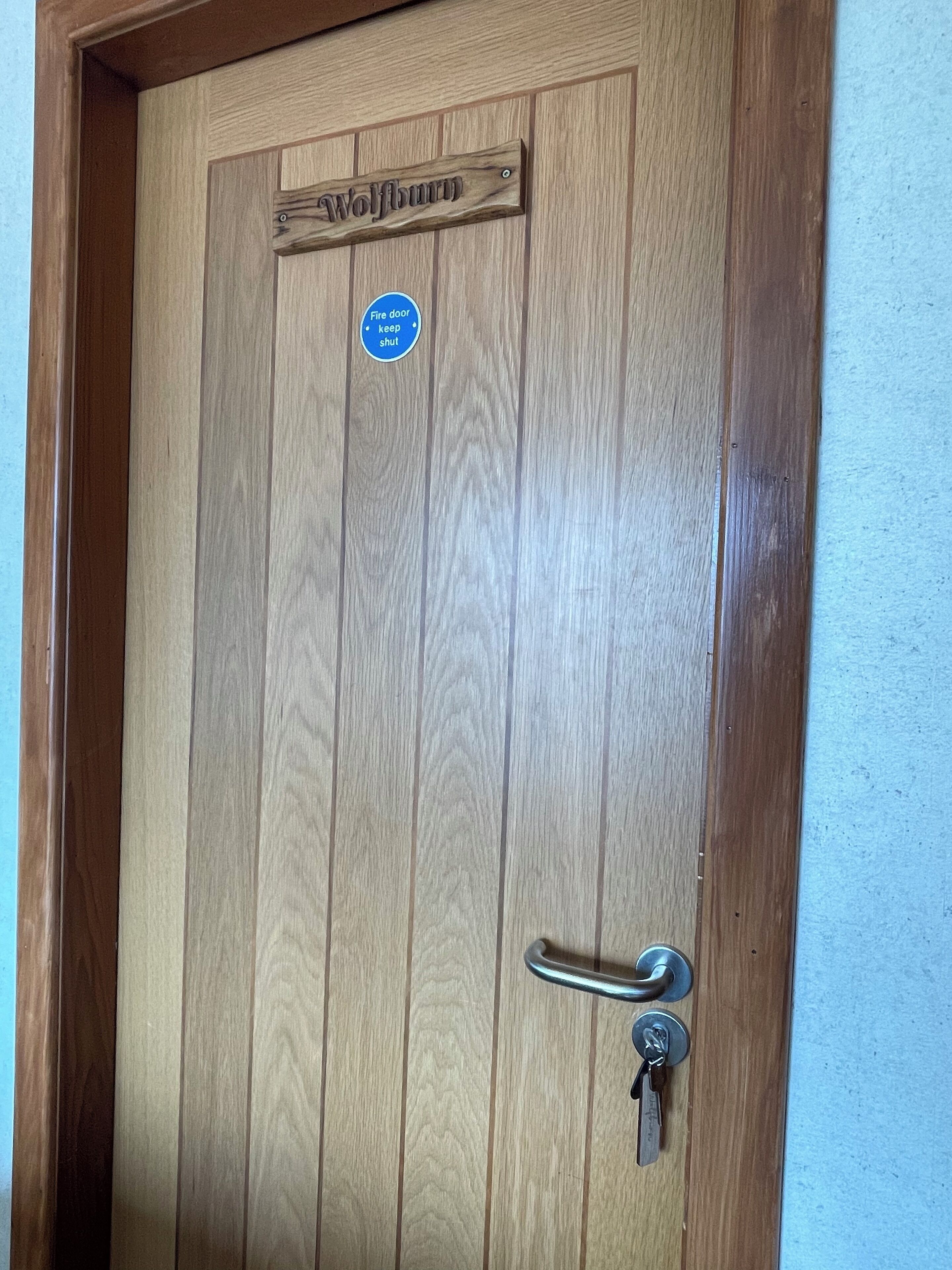 Una puerta de madera con una placa que dice "Wolflamb" y un letrero azul que indica "Puerta cortafuegos. Mantener cerrada."