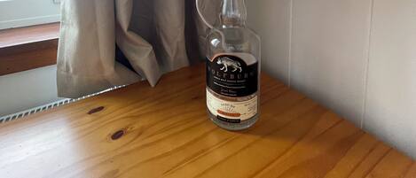 A bottle of Wolfburn Cherry Bay whisky on a wooden table with a grey textured lamp beside it.